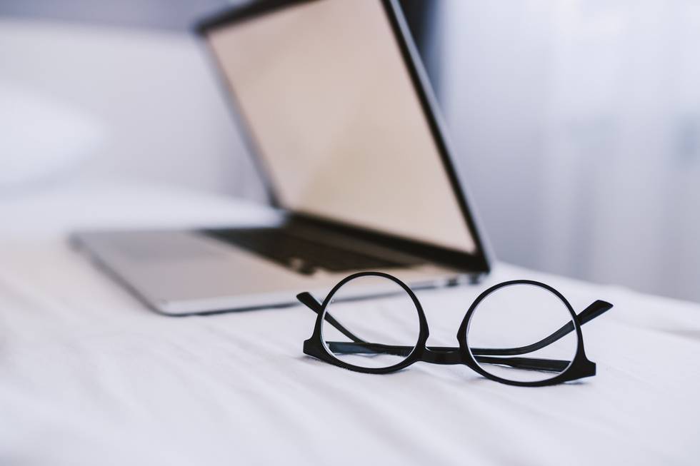 Picture of eyeglasses and laptop on bed in bedroom. Selective fo